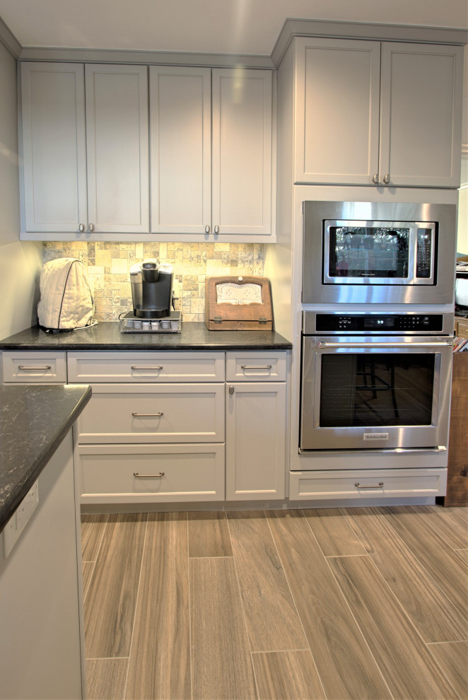 ダラスにあるエクレクティックスタイルのおしゃれなキッチン (白いキャビネット、マルチカラーのキッチンパネル、ライムストーンのキッチンパネル、シルバーの調理設備、茶色い床、黒いキッチンカウンター) の写真