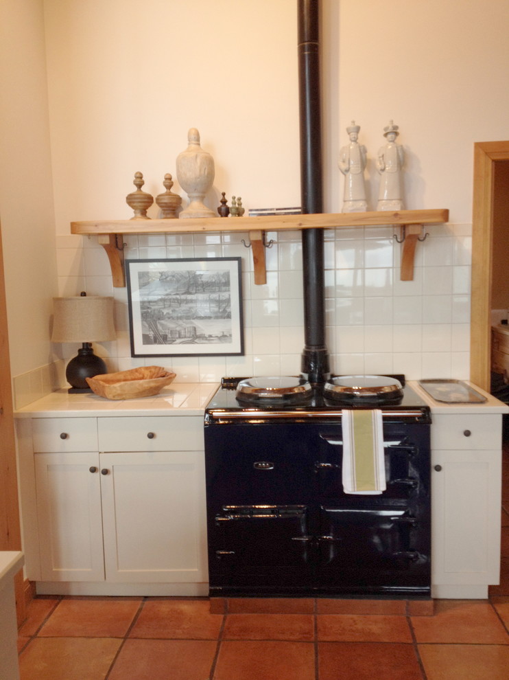 Eklektisk inredning av ett kök, med luckor med infälld panel, vita skåp, kaklad bänkskiva, vitt stänkskydd och svarta vitvaror