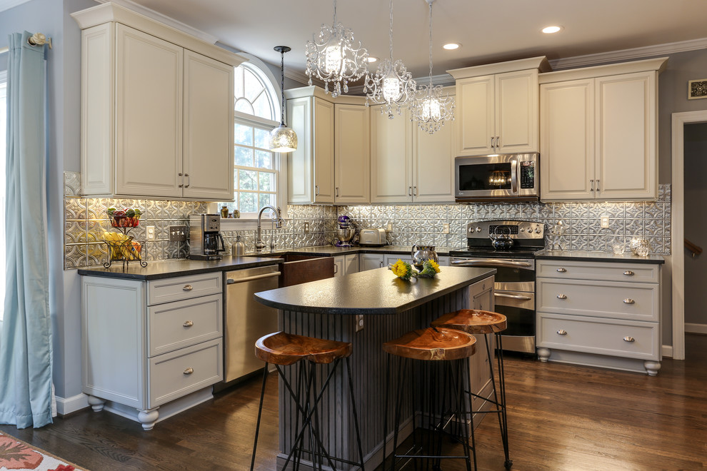 Inspiration for a mid-sized eclectic l-shaped eat-in kitchen remodel in Raleigh with a farmhouse sink, raised-panel cabinets, gray cabinets, granite countertops, gray backsplash, metal backsplash, stainless steel appliances and an island