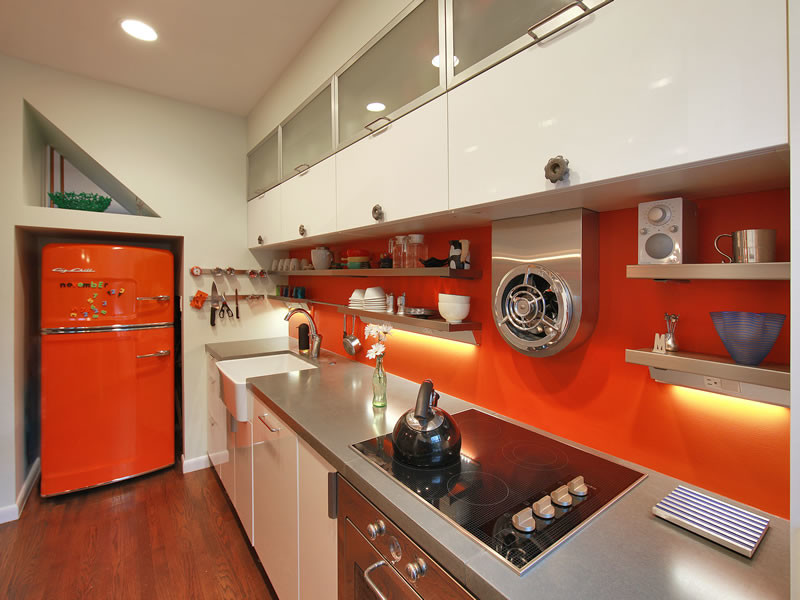 This is an example of a small eclectic galley enclosed kitchen in DC Metro with a belfast sink, flat-panel cabinets, white cabinets, concrete worktops, orange splashback, stainless steel appliances, medium hardwood flooring and brown floors.