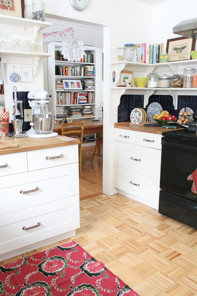 Idées déco pour une cuisine éclectique fermée avec un plan de travail en bois, un placard sans porte, des portes de placard blanches, une crédence bleue et un électroménager noir.