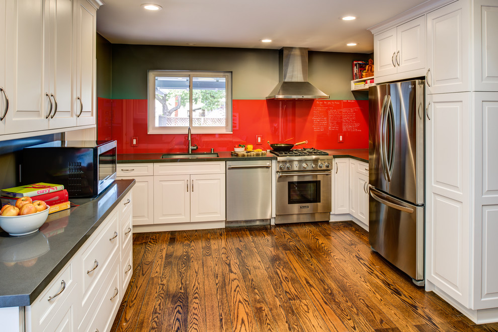 Eklektisk inredning av ett litet kök, med en enkel diskho, luckor med upphöjd panel, vita skåp, bänkskiva i kvarts, rött stänkskydd, glaspanel som stänkskydd, rostfria vitvaror och mellanmörkt trägolv