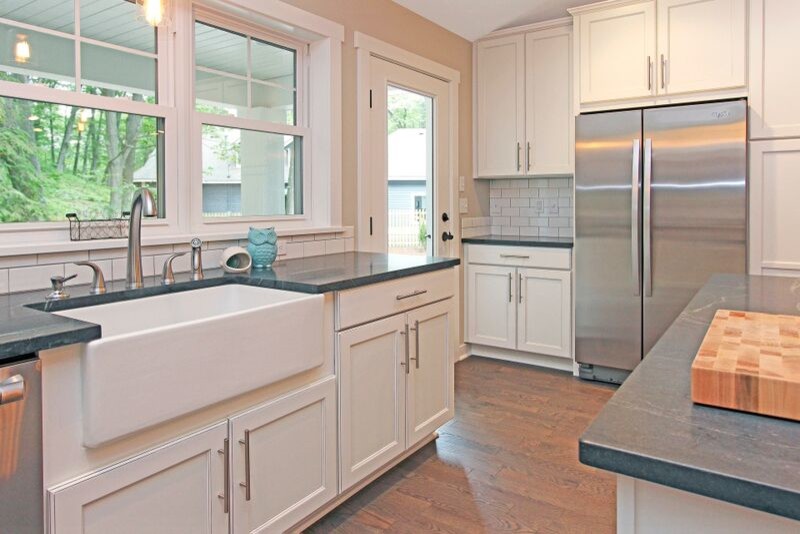 Photo of a bohemian galley kitchen in Grand Rapids with a belfast sink, raised-panel cabinets, white cabinets, soapstone worktops, white splashback, metro tiled splashback, stainless steel appliances, medium hardwood flooring and an island.