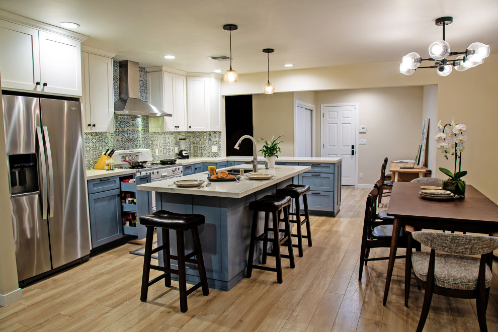 Eklektisk inredning av ett mellanstort vit vitt kök, med en undermonterad diskho, skåp i shakerstil, blå skåp, bänkskiva i kvarts, blått stänkskydd, stänkskydd i porslinskakel, rostfria vitvaror, laminatgolv, en köksö och beiget golv