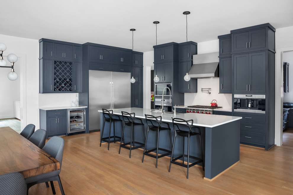 This is an example of a large retro kitchen/diner in Houston with a belfast sink, blue cabinets, white splashback, stainless steel appliances, medium hardwood flooring, an island, white worktops and shaker cabinets.