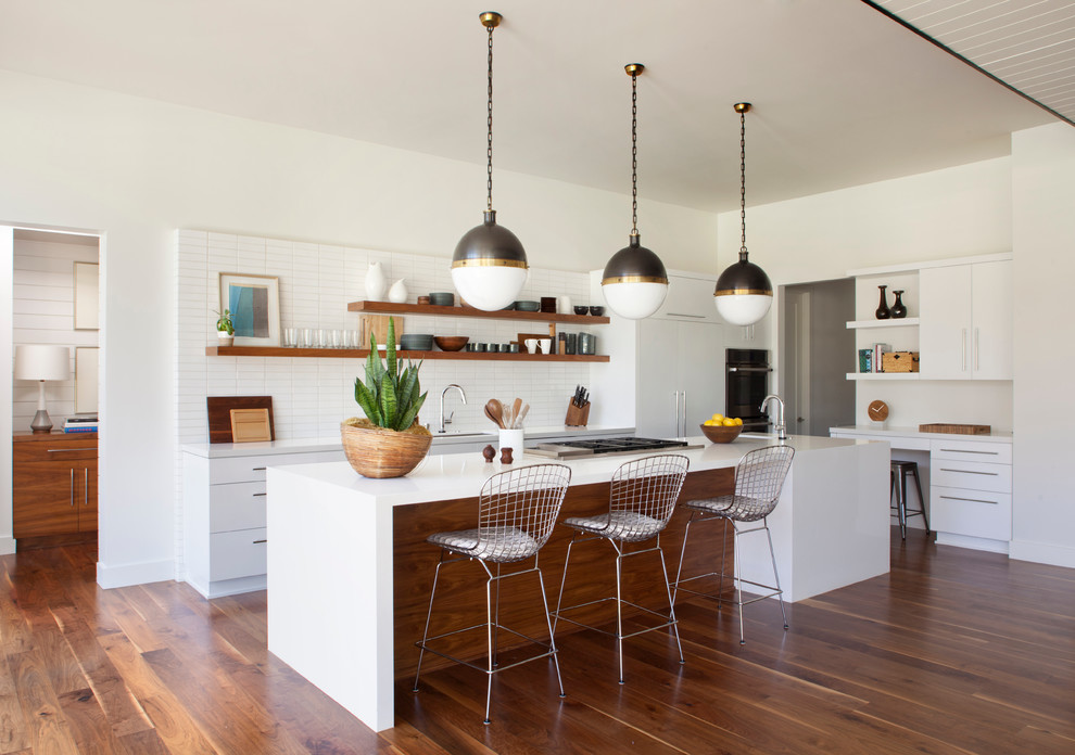 Design ideas for a medium sized midcentury l-shaped open plan kitchen in Los Angeles with flat-panel cabinets, white cabinets, engineered stone countertops, white splashback, ceramic splashback, integrated appliances, medium hardwood flooring and an island.