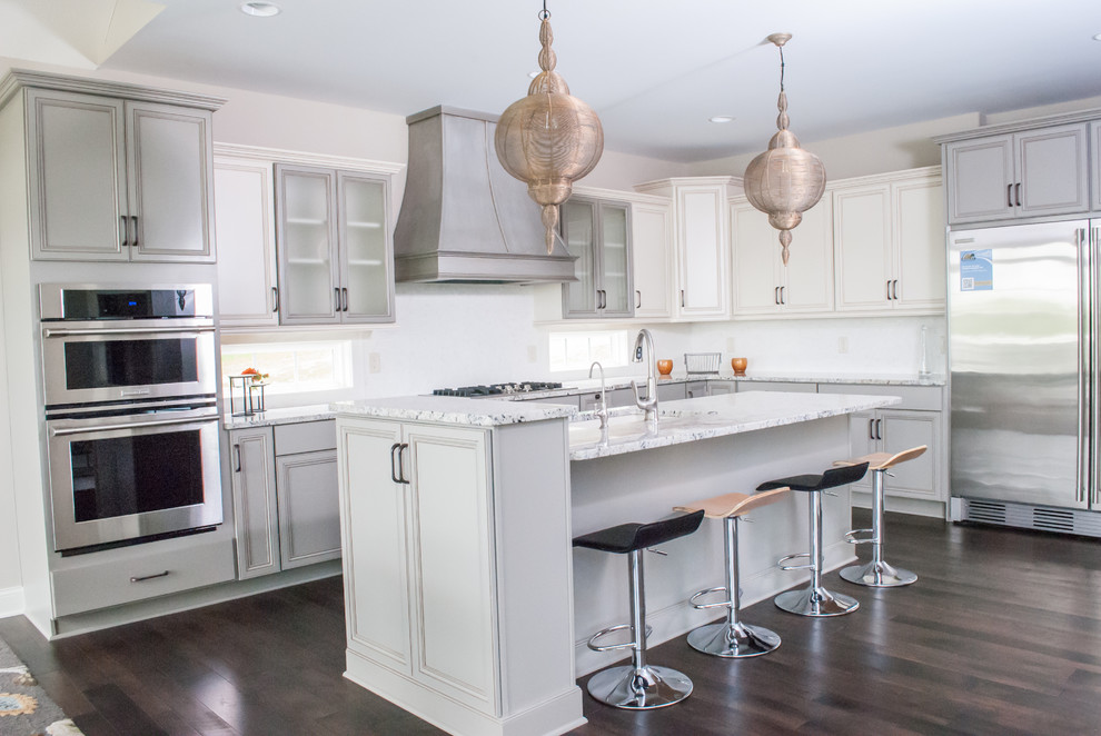 Example of an eclectic l-shaped dark wood floor eat-in kitchen design in Cleveland with an integrated sink, raised-panel cabinets, white cabinets, granite countertops, white backsplash, glass tile backsplash, stainless steel appliances and an island