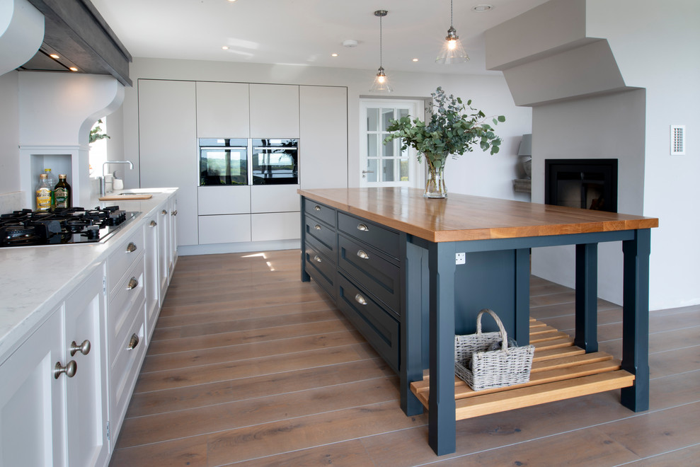 Foto på ett mellanstort eklektiskt vit kök, med en integrerad diskho, skåp i shakerstil, vita skåp, bänkskiva i kvartsit, vitt stänkskydd, stänkskydd i sten, svarta vitvaror, mellanmörkt trägolv, en köksö och grått golv