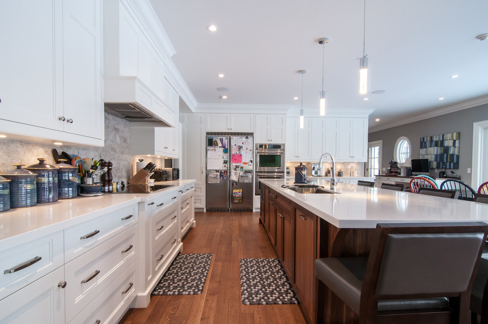 Bild på ett stort eklektiskt kök, med en undermonterad diskho, skåp i shakerstil, vita skåp, bänkskiva i kvarts, grått stänkskydd, stänkskydd i porslinskakel, rostfria vitvaror, mellanmörkt trägolv och en köksö