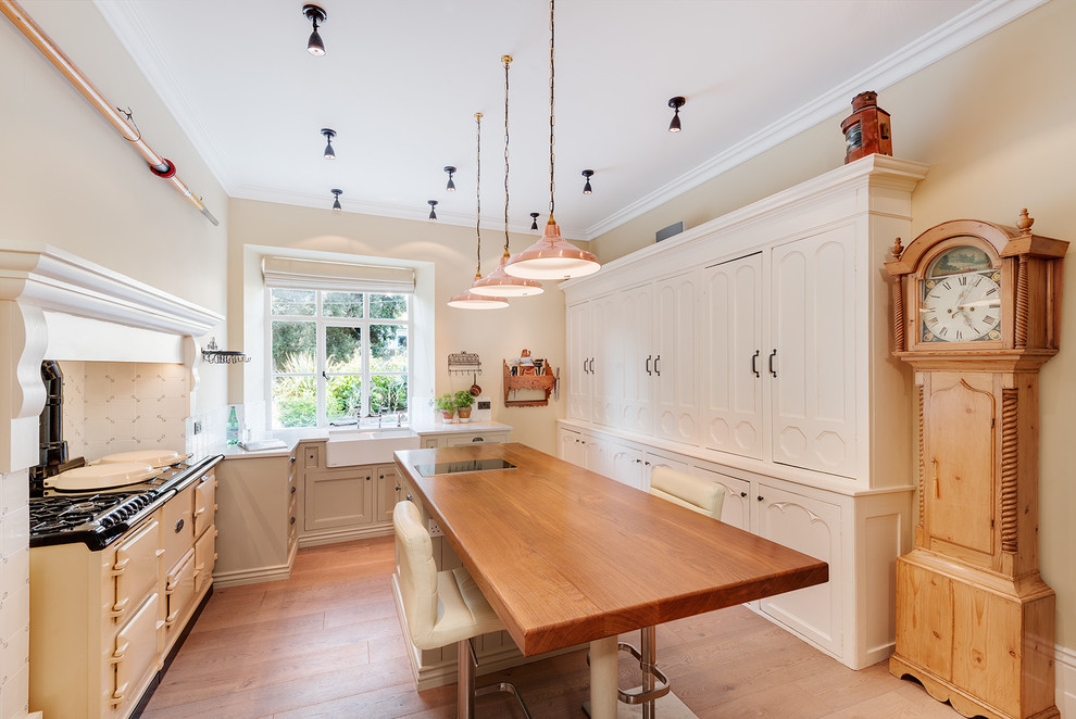 Klassische Küche in L-Form mit Landhausspüle, Schrankfronten mit vertiefter Füllung, hellem Holzboden, Kücheninsel und weißen Elektrogeräten in Devon