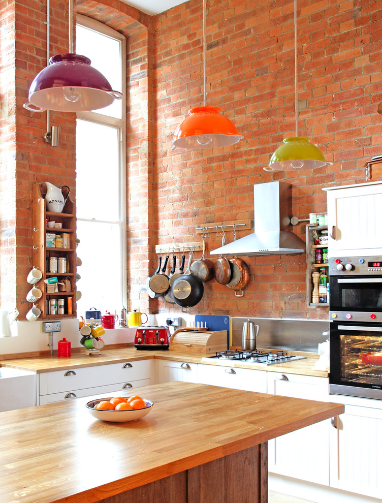 Kitchen - mid-sized eclectic l-shaped kitchen idea in London with shaker cabinets, white cabinets, wood countertops, metallic backsplash, stainless steel appliances and an island
