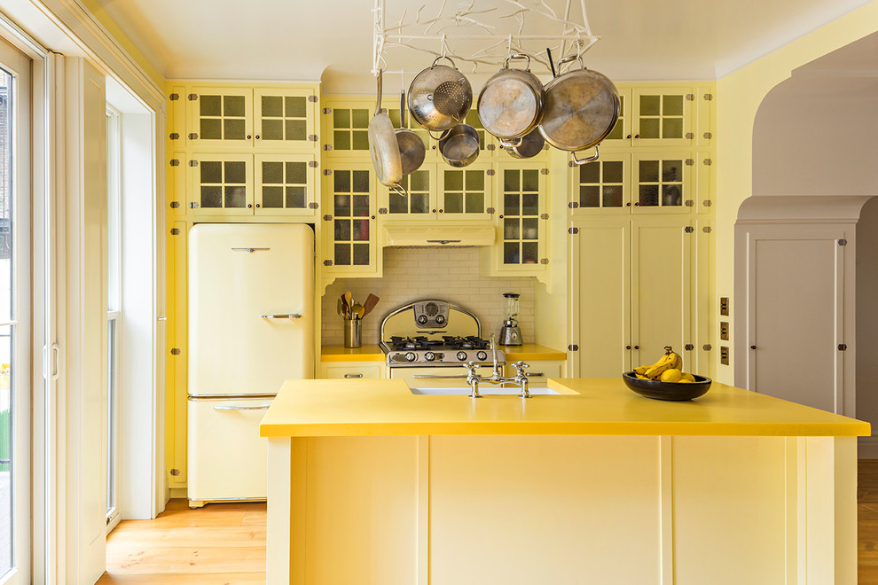 Foto på ett mellanstort vintage gul kök, med gula skåp, bänkskiva i återvunnet glas, vitt stänkskydd, färgglada vitvaror, en köksö, luckor med glaspanel, stänkskydd i tunnelbanekakel och ljust trägolv