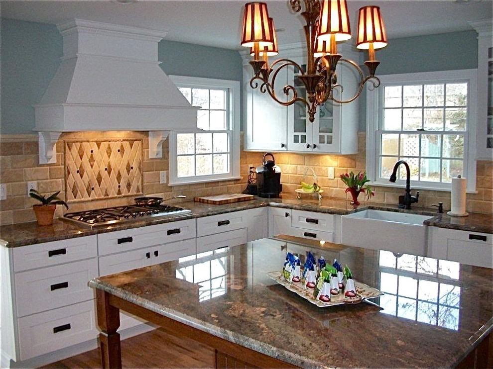Inspiration for a mid-sized timeless u-shaped medium tone wood floor eat-in kitchen remodel in New York with a farmhouse sink, shaker cabinets, white cabinets, granite countertops, beige backsplash, stone tile backsplash, stainless steel appliances and an island