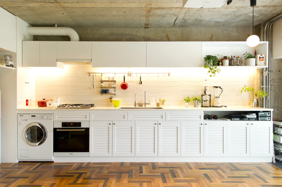 This is an example of a large single-wall open plan kitchen in Tokyo with a submerged sink, louvered cabinets, white cabinets, white splashback, matchstick tiled splashback, white appliances, medium hardwood flooring and no island.