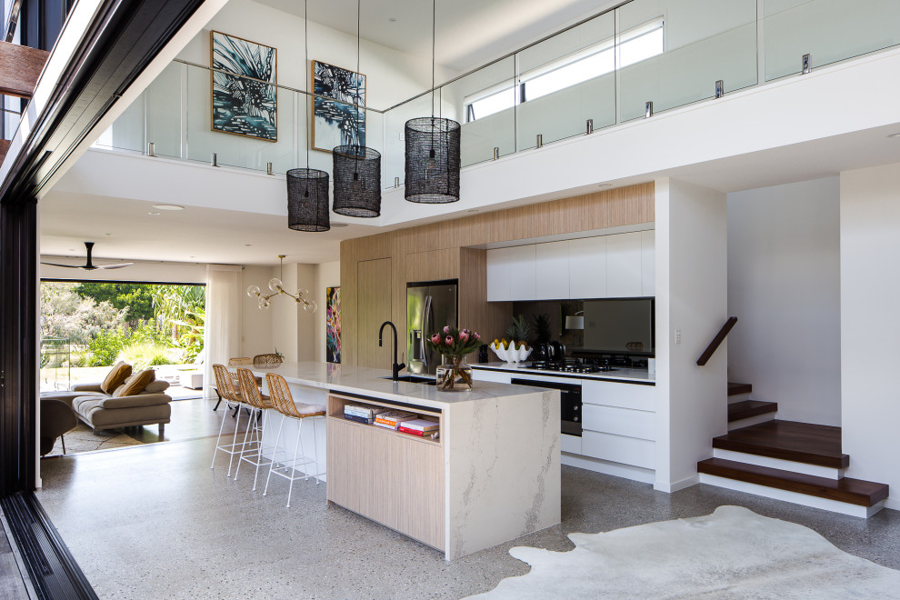 Foto på ett funkis vit kök, med en undermonterad diskho, släta luckor, vita skåp, svart stänkskydd, rostfria vitvaror, betonggolv, en köksö och grått golv