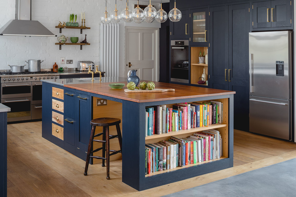 Foto på ett lantligt kök, med en integrerad diskho, skåp i shakerstil, blå skåp, träbänkskiva, vitt stänkskydd, stänkskydd i tegel, rostfria vitvaror, ljust trägolv, en köksö och beiget golv