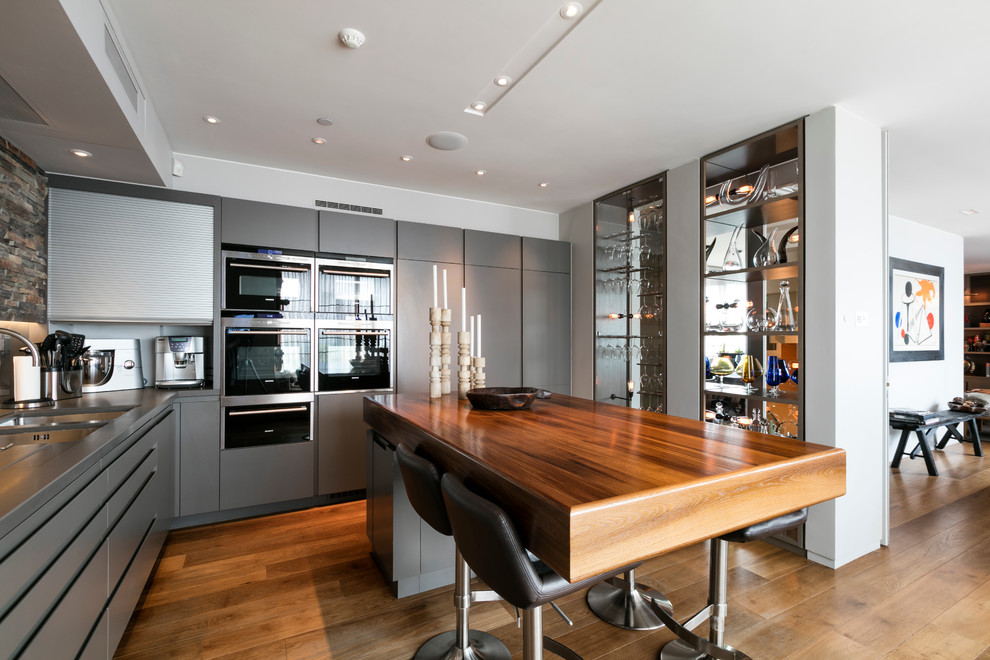 Example of a mid-century modern l-shaped dark wood floor open concept kitchen design in London with a double-bowl sink, flat-panel cabinets, gray cabinets and an island