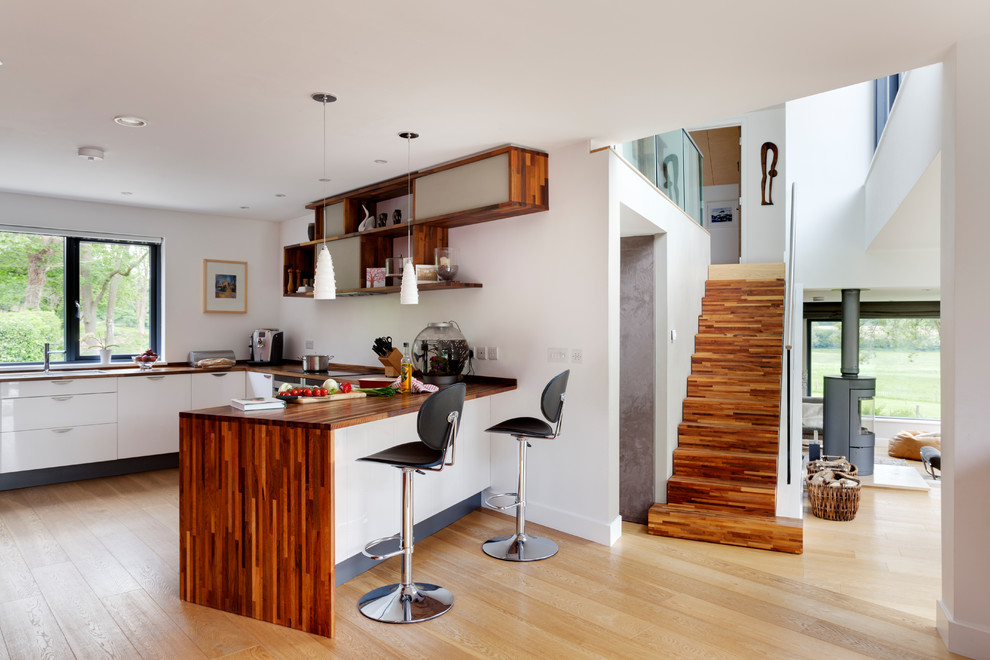 Photo of a contemporary u-shaped open plan kitchen in Kent with flat-panel cabinets, white cabinets, light hardwood flooring and a breakfast bar.
