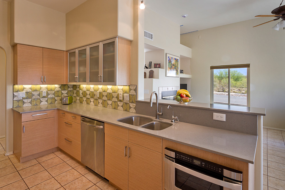 Example of a mid-sized minimalist galley porcelain tile open concept kitchen design in Phoenix with an undermount sink, glass-front cabinets, light wood cabinets, glass countertops, green backsplash, glass sheet backsplash, stainless steel appliances and no island