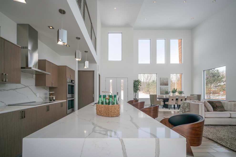 Example of a large danish galley porcelain tile and brown floor open concept kitchen design in Detroit with an undermount sink, flat-panel cabinets, light wood cabinets, quartz countertops, white backsplash, stone slab backsplash, stainless steel appliances, an island and white countertops