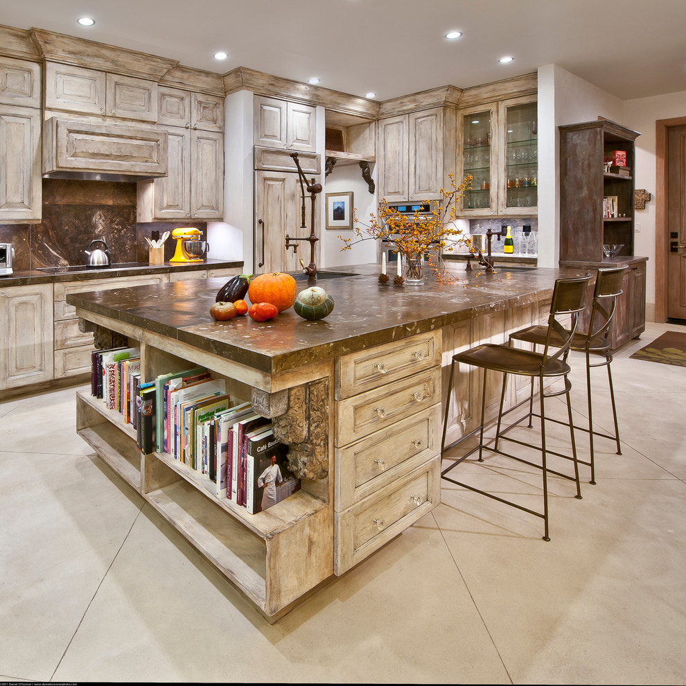Example of a tuscan galley concrete floor kitchen design in Denver with raised-panel cabinets, distressed cabinets, brown backsplash, paneled appliances and an island