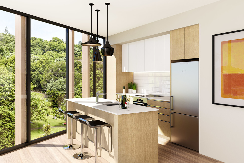 Moderne Küche mit Unterbauwaschbecken, flächenbündigen Schrankfronten, hellen Holzschränken, Küchenrückwand in Weiß, Rückwand aus Metrofliesen, Küchengeräten aus Edelstahl, braunem Holzboden und Kücheninsel in Auckland