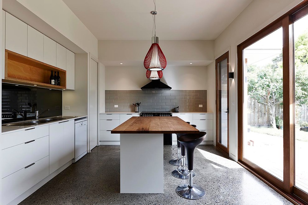 Modern inredning av ett mellanstort l-kök, med en dubbel diskho, släta luckor, träbänkskiva, grått stänkskydd, stänkskydd i tunnelbanekakel, svarta vitvaror, betonggolv och en köksö