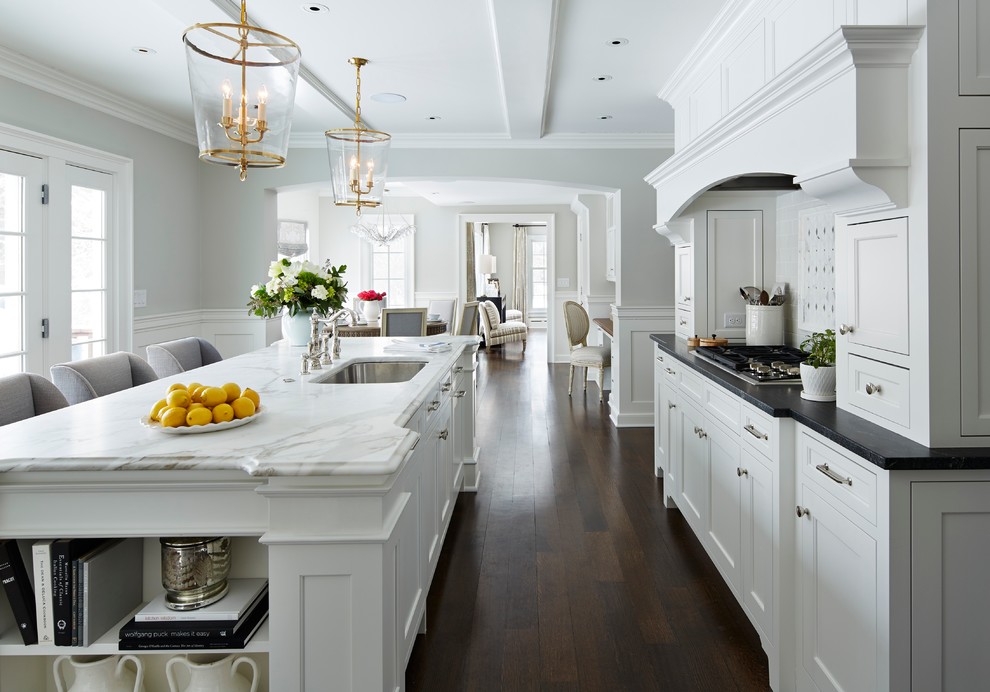 Example of a mid-sized classic l-shaped dark wood floor eat-in kitchen design in Minneapolis with recessed-panel cabinets, white cabinets, marble countertops, white backsplash, stainless steel appliances, an undermount sink and an island