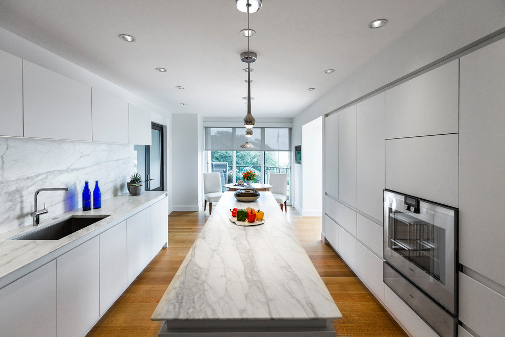Bild på ett mellanstort funkis kök, med en enkel diskho, släta luckor, vita skåp, marmorbänkskiva, grått stänkskydd, stänkskydd i marmor, rostfria vitvaror, mellanmörkt trägolv, en köksö och brunt golv