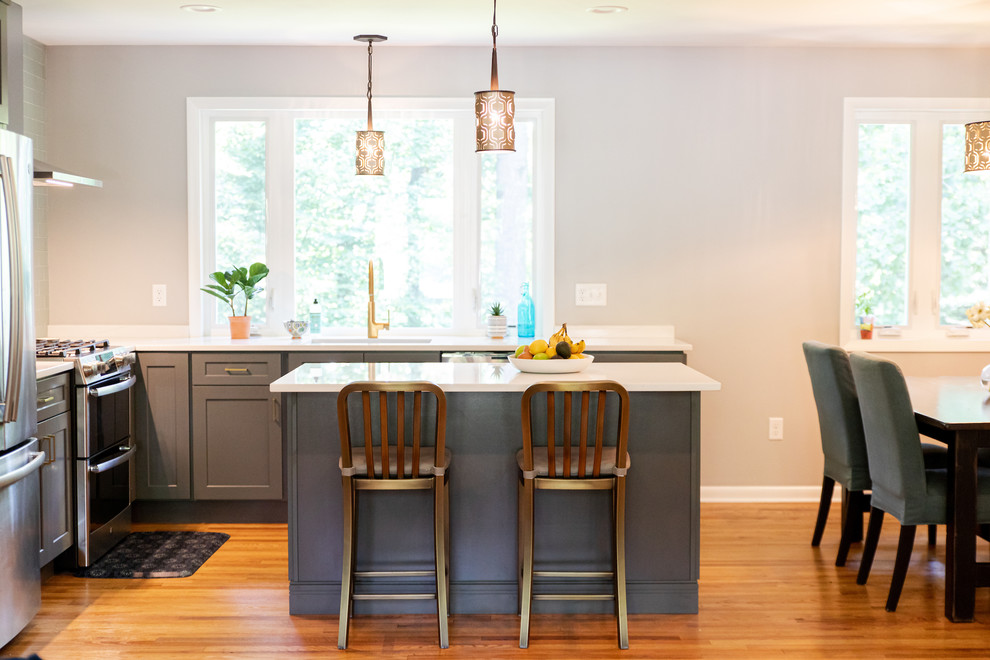 Bild på ett litet amerikanskt vit vitt kök, med en nedsänkt diskho, blå skåp, bänkskiva i kvarts, flerfärgad stänkskydd, stänkskydd i glaskakel, rostfria vitvaror, ljust trägolv, en köksö och brunt golv