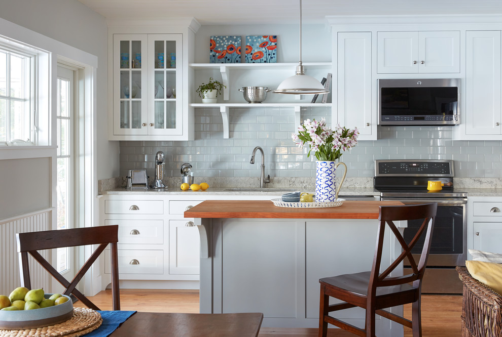 Example of a beach style light wood floor eat-in kitchen design in Portland Maine with an undermount sink, shaker cabinets, white cabinets, gray backsplash, subway tile backsplash, stainless steel appliances, an island and gray countertops