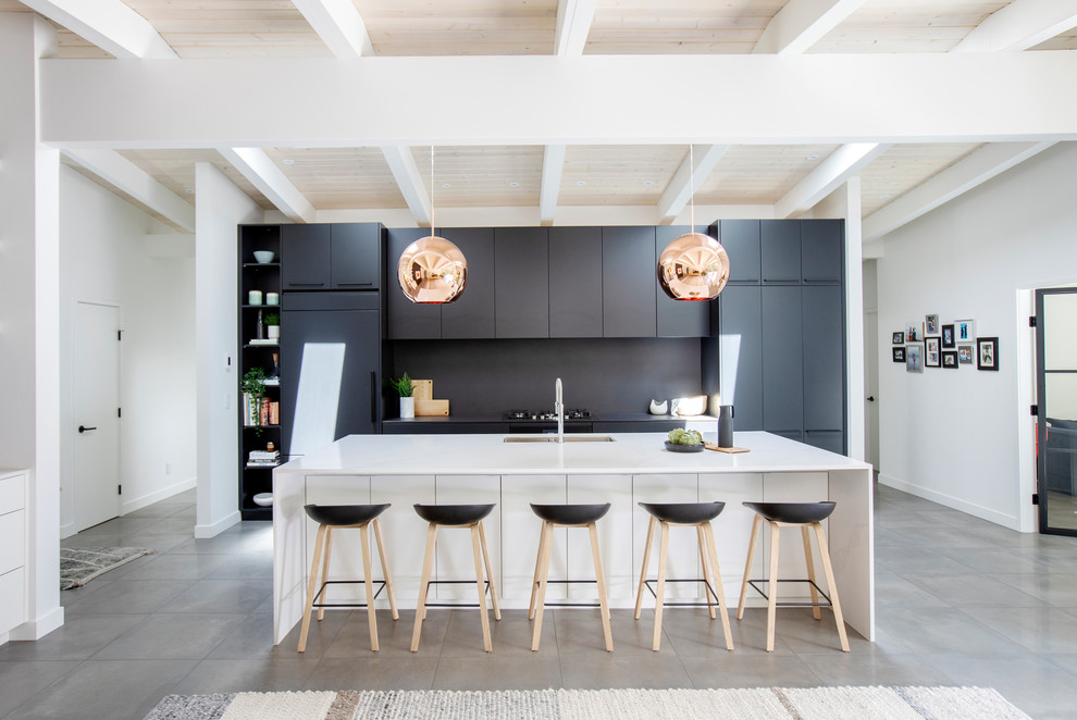 Photo of a large midcentury single-wall open plan kitchen in Vancouver with a submerged sink, flat-panel cabinets, black cabinets, black splashback, integrated appliances, an island, grey floors, black worktops, engineered stone countertops and concrete flooring.