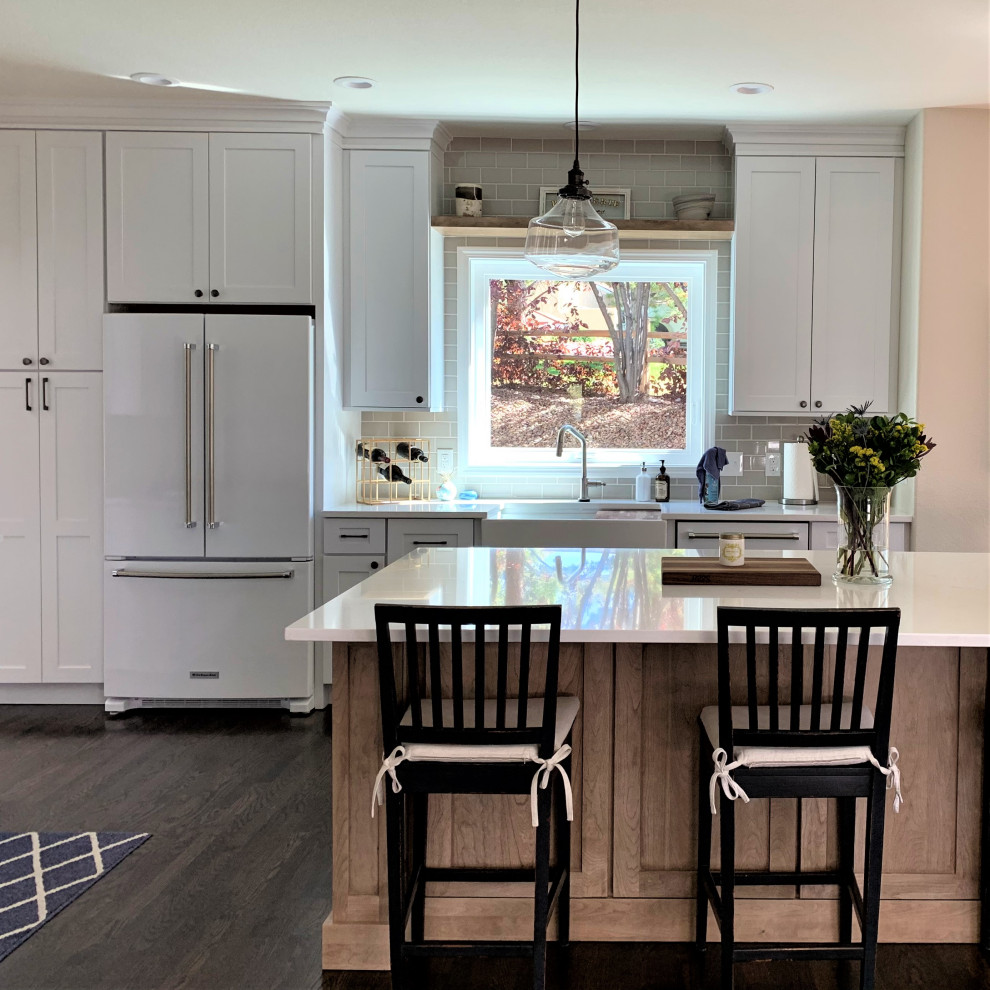 Design ideas for a large classic l-shaped open plan kitchen in Denver with a belfast sink, shaker cabinets, white cabinets, engineered stone countertops, glass tiled splashback, white appliances, an island and white worktops.