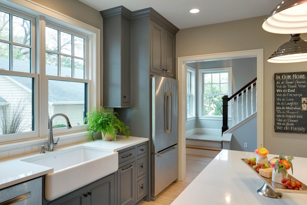 Inspiration for a large cottage l-shaped light wood floor and beige floor open concept kitchen remodel in Minneapolis with a farmhouse sink, shaker cabinets, gray cabinets, solid surface countertops, white backsplash, subway tile backsplash, stainless steel appliances and an island