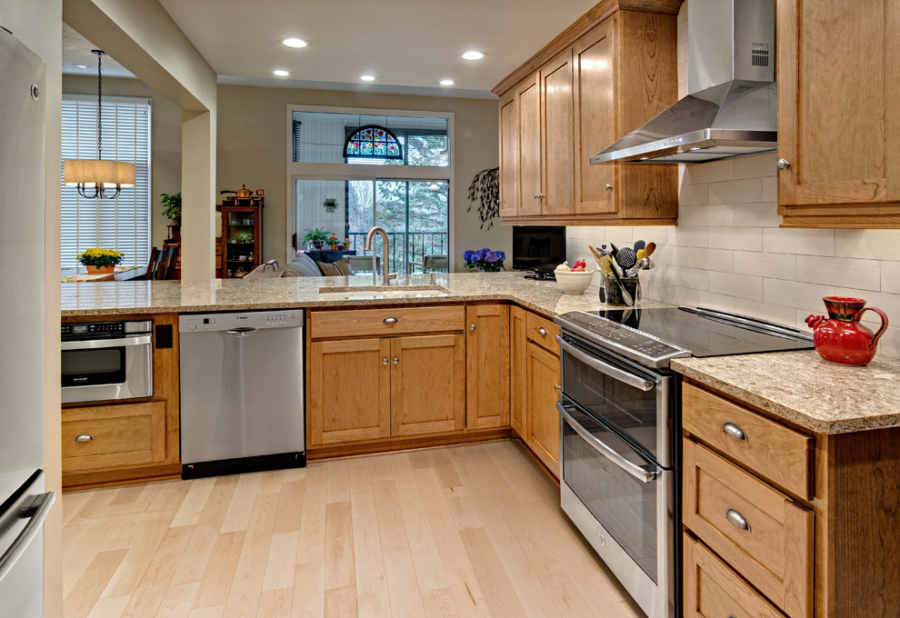 Klassisk inredning av ett mellanstort kök, med en undermonterad diskho, luckor med infälld panel, skåp i mellenmörkt trä, bänkskiva i kvarts, beige stänkskydd, stänkskydd i porslinskakel, rostfria vitvaror, ljust trägolv, en halv köksö och beiget golv