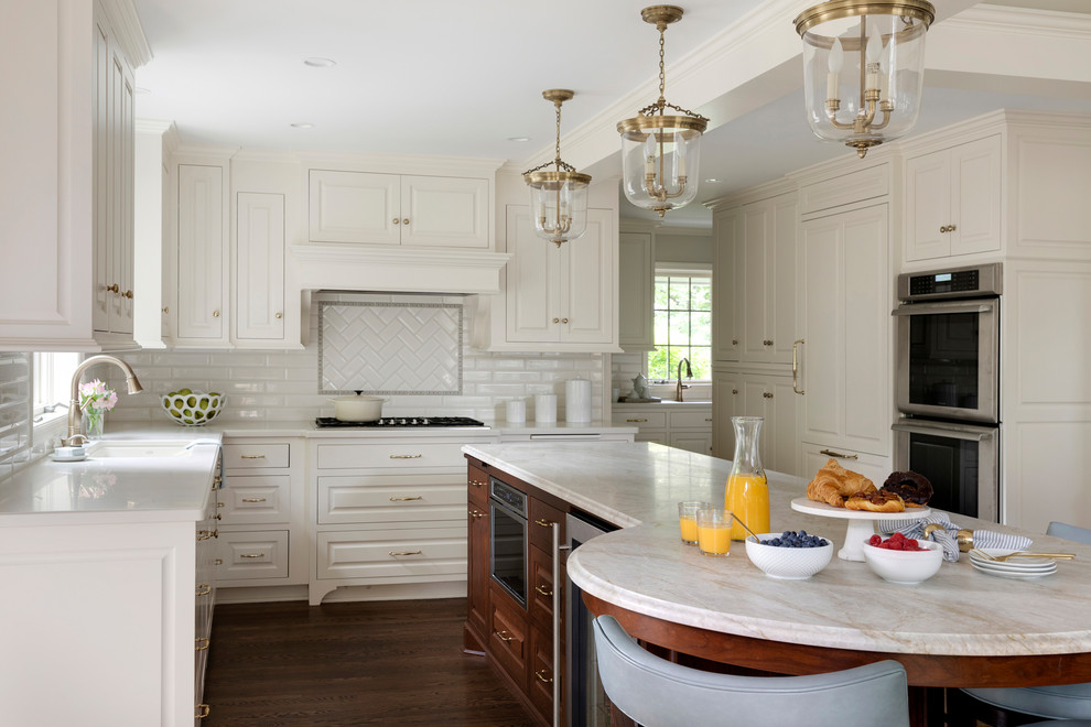 Exempel på ett stort klassiskt vit vitt kök, med luckor med upphöjd panel, vita skåp, marmorbänkskiva, vitt stänkskydd, stänkskydd i tunnelbanekakel, integrerade vitvaror, mörkt trägolv, en köksö och brunt golv