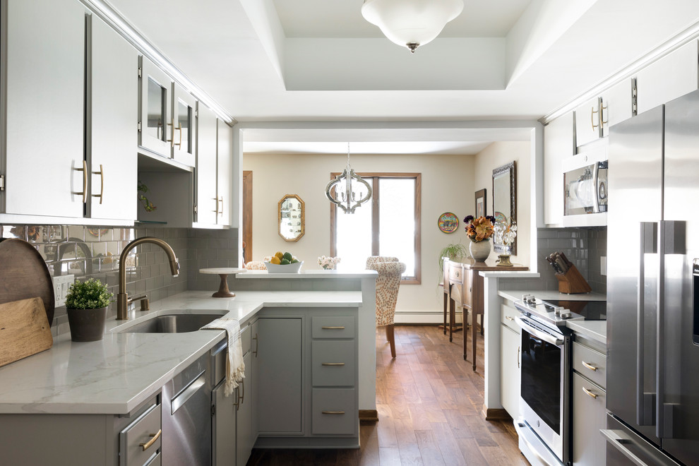 Mid-sized transitional galley medium tone wood floor and brown floor eat-in kitchen photo in Minneapolis with an undermount sink, flat-panel cabinets, gray cabinets, quartz countertops, gray backsplash, glass tile backsplash, stainless steel appliances, a peninsula and white countertops