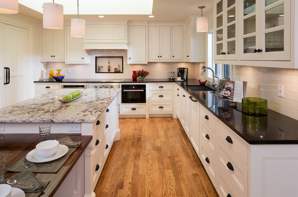 Kitchen pantry - mid-sized modern u-shaped medium tone wood floor kitchen pantry idea in Minneapolis with an undermount sink, glass-front cabinets, white cabinets, granite countertops, white backsplash, subway tile backsplash, black appliances and an island