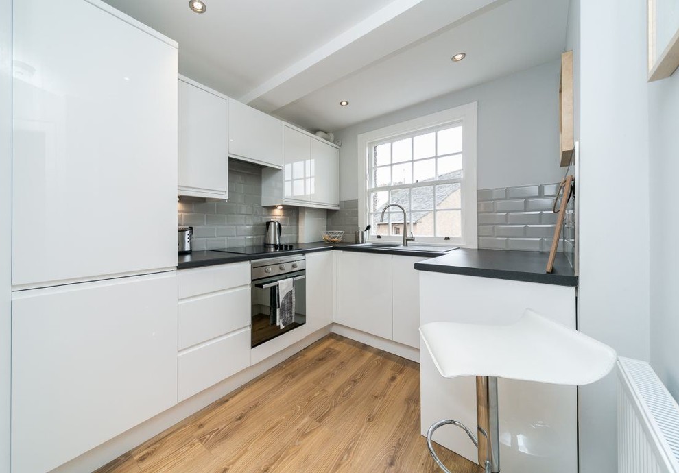 Inspiration for a small contemporary u-shaped enclosed kitchen in Edinburgh with flat-panel cabinets, white cabinets, laminate countertops, grey splashback, mosaic tiled splashback, integrated appliances and laminate floors.