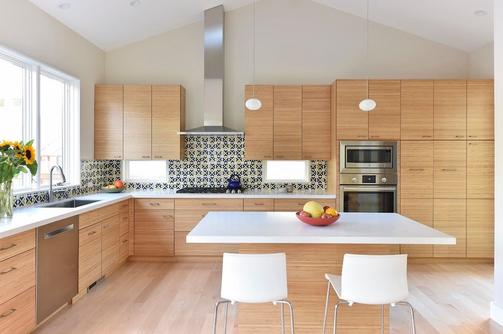 Modern inredning av ett stort kök, med en undermonterad diskho, släta luckor, rostfria vitvaror, ljust trägolv, en köksö, skåp i mellenmörkt trä, bänkskiva i kvartsit, flerfärgad stänkskydd och stänkskydd i keramik
