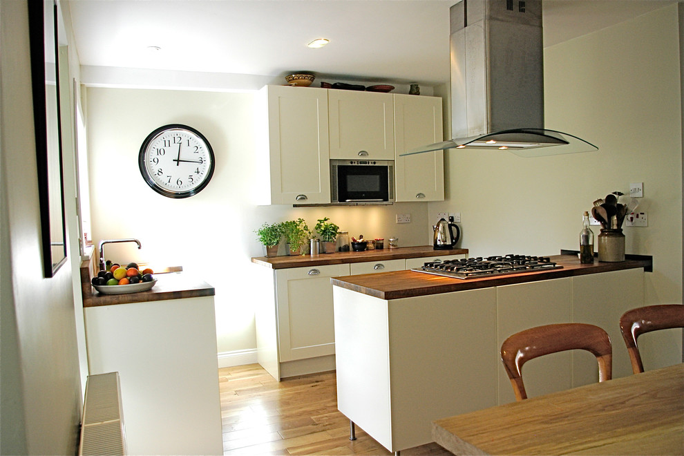 Foto på ett mellanstort vintage kök, med en undermonterad diskho, skåp i shakerstil, vita skåp, träbänkskiva, rostfria vitvaror, ljust trägolv och en halv köksö