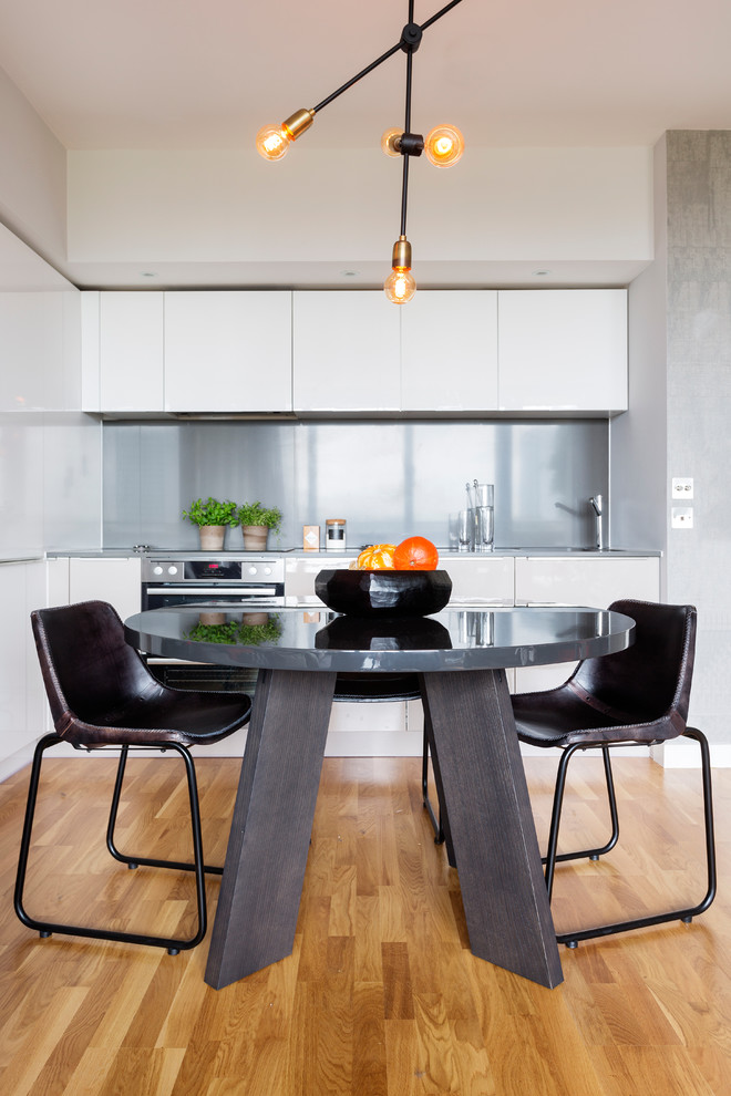 Idéer för ett stort modernt kök, med en enkel diskho, släta luckor, vita skåp, stänkskydd med metallisk yta och mellanmörkt trägolv