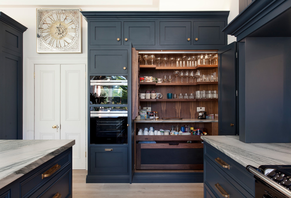 Exempel på ett klassiskt vit vitt kök och matrum, med luckor med profilerade fronter, marmorbänkskiva, spegel som stänkskydd, rostfria vitvaror, ljust trägolv och en köksö