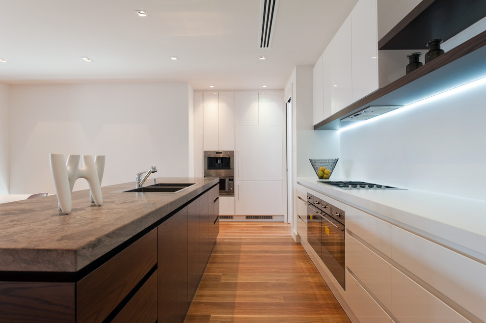 Inspiration for a medium sized contemporary kitchen/diner in Adelaide with a double-bowl sink, flat-panel cabinets, dark wood cabinets, limestone worktops, white splashback, stainless steel appliances and an island.