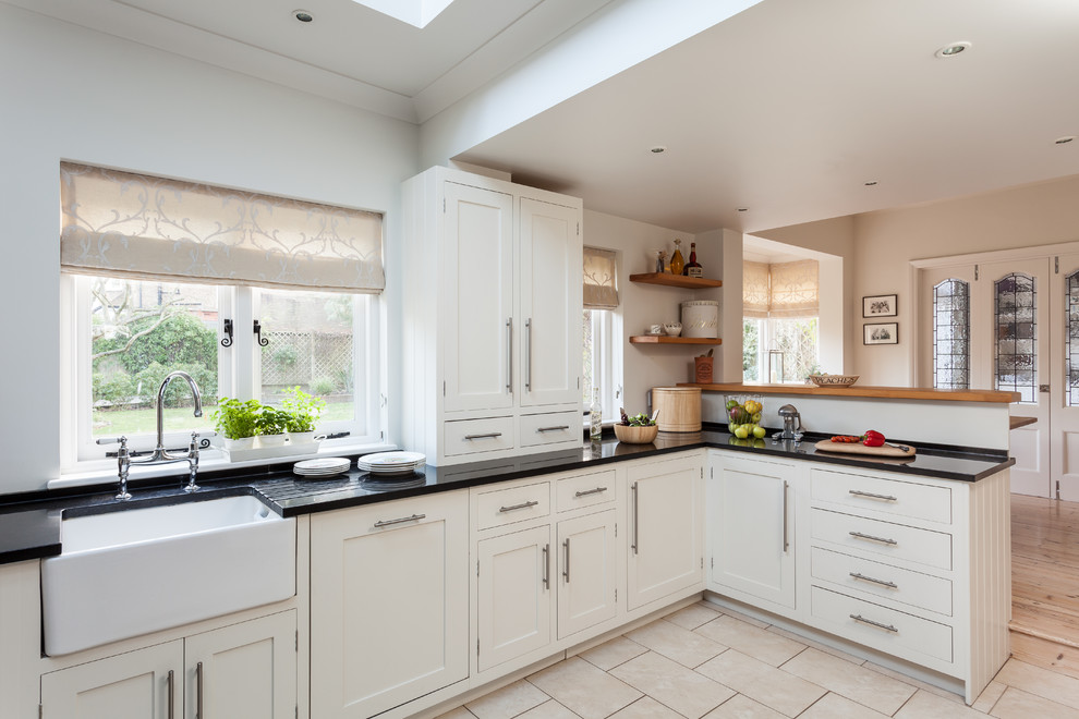 Inspiration for a medium sized traditional kitchen in Surrey with a belfast sink, shaker cabinets, white cabinets, laminate countertops, stainless steel appliances, limestone flooring and a breakfast bar.