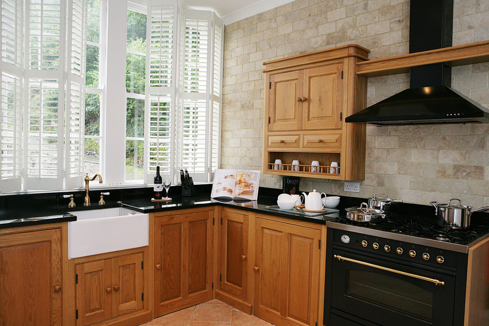 Geschlossene Landhausstil Küche in L-Form mit profilierten Schrankfronten, hellbraunen Holzschränken, Onyx-Arbeitsplatte und Küchenrückwand in Schwarz in Sonstige