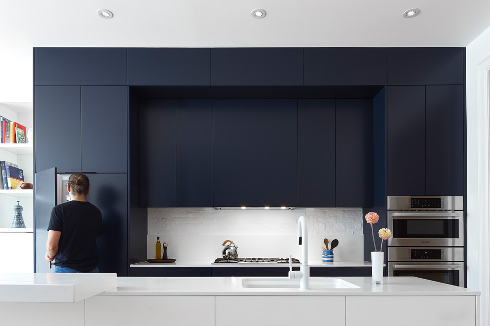 Foto di una cucina design con lavello sottopiano, ante lisce, ante nere, paraspruzzi bianco, elettrodomestici in acciaio inossidabile e top bianco