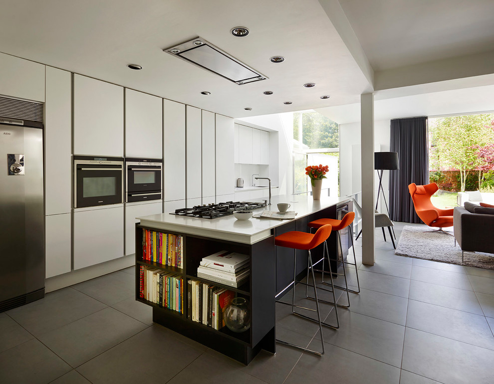 Exemple d'une cuisine ouverte parallèle moderne avec un placard à porte plane, des portes de placard blanches, un électroménager en acier inoxydable, îlot et un sol gris.