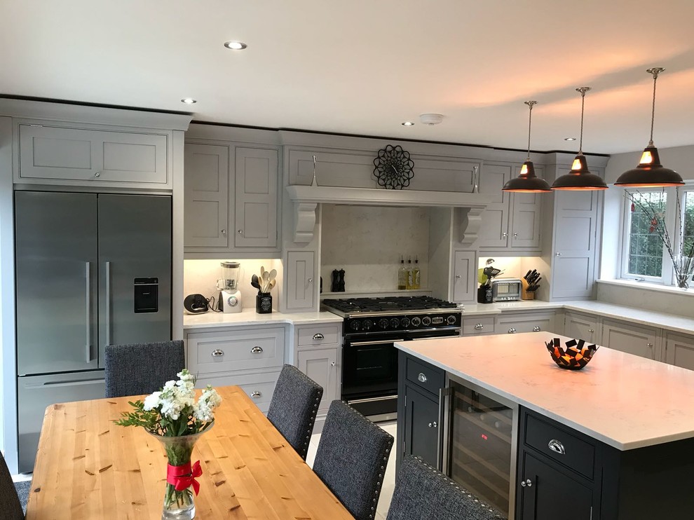 Photo of a large classic l-shaped kitchen/diner in Essex with a belfast sink, shaker cabinets, grey cabinets, marble worktops, white splashback, stainless steel appliances, an island and beige floors.
