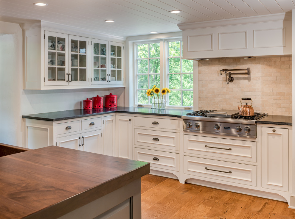 Eat-in kitchen - small farmhouse l-shaped light wood floor and brown floor eat-in kitchen idea in Philadelphia with a farmhouse sink, recessed-panel cabinets, white cabinets, granite countertops, beige backsplash, ceramic backsplash, stainless steel appliances, an island and black countertops